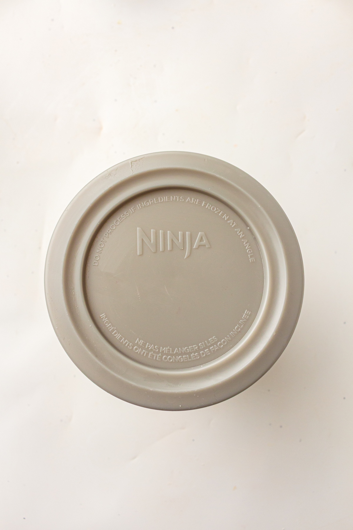 Close-up of a Ninja Creami container lid with embossed safety instructions, warning not to process ingredients frozen at an angle.