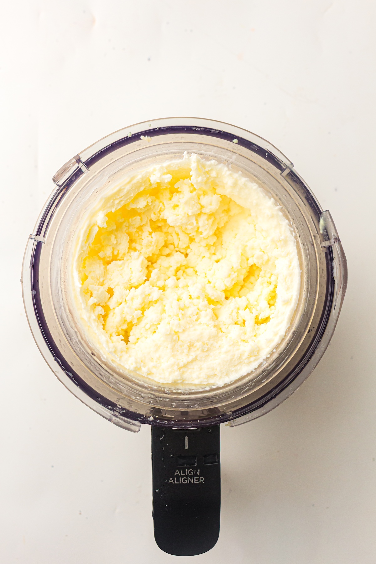 Overhead shot of a Ninja Creami container filled with pale yellow, creamy mixture, with a black handle labeled 'ALIGN ALIGNER' visible.