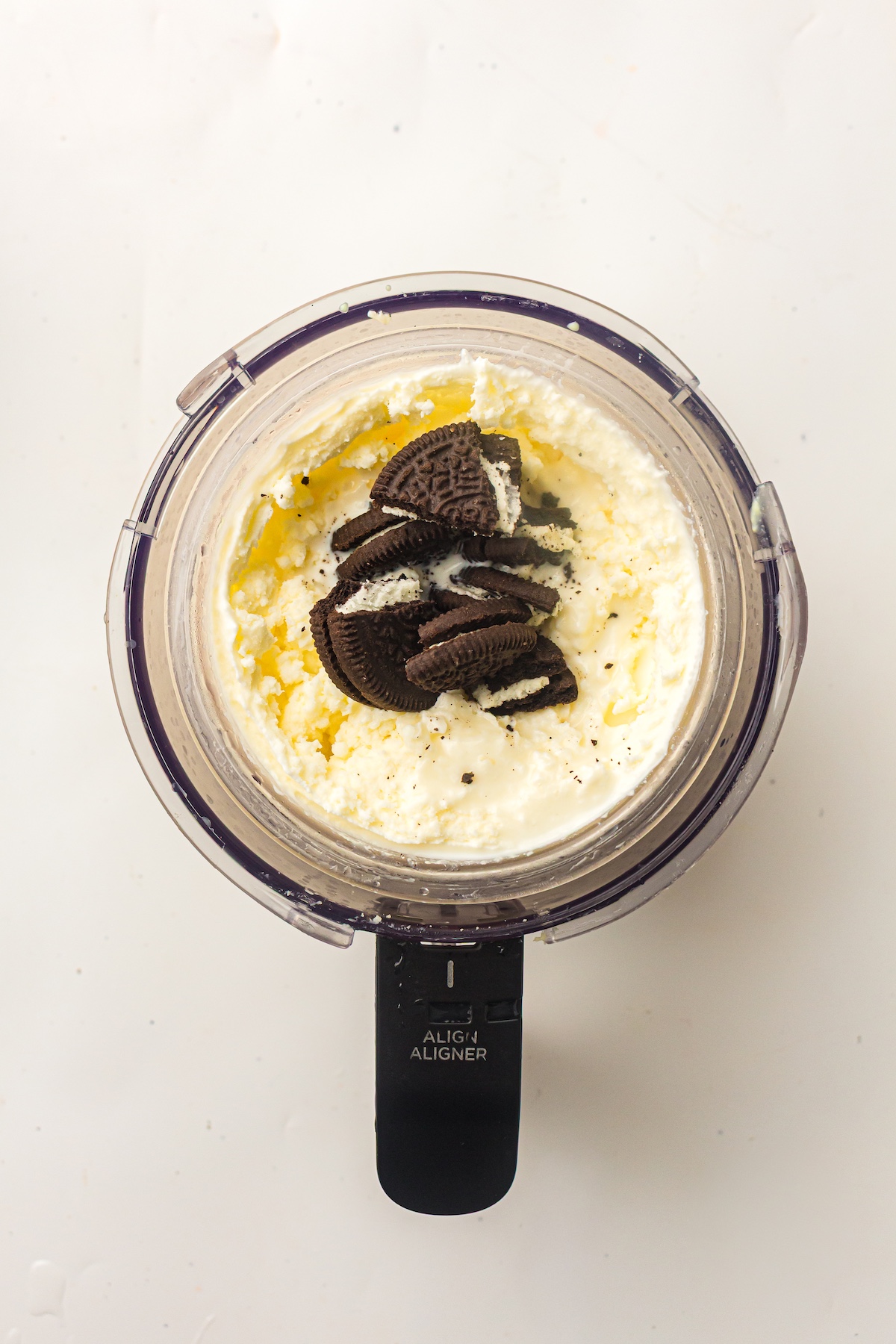 Top-down shot of a clear container filled with light creamy base, topped with dark chocolate Oreo cookies, with 'ALIGN ALIGNER' text on the handle.