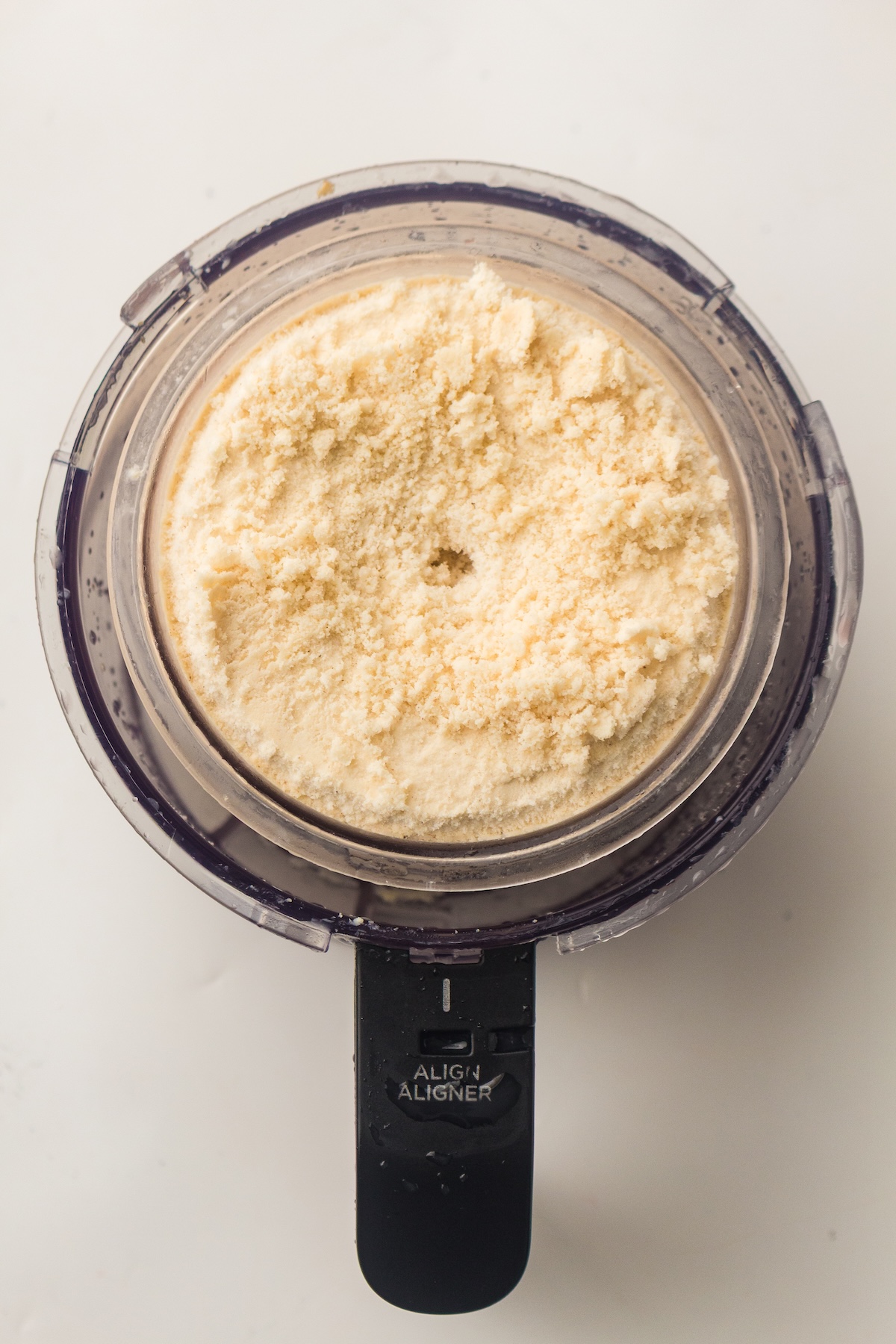 Top-down view of a clear kitchen appliance container filled with light beige powder, with a black handle labeled 'ALIGN ALIGNER,' set against a plain white background.