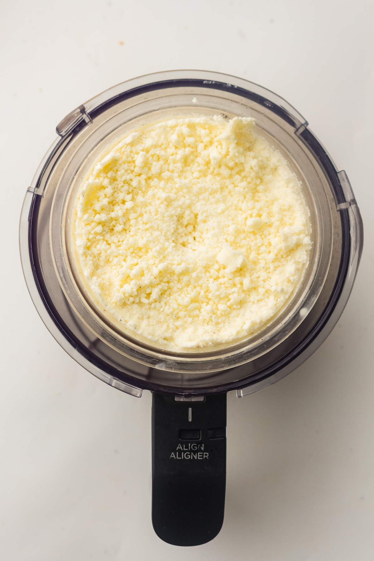 Top-down view of a clear container filled with a pale yellow, granular substance with dark specks, featuring a black handle labeled 'ALIGN ALIGNER,' set on a white background.