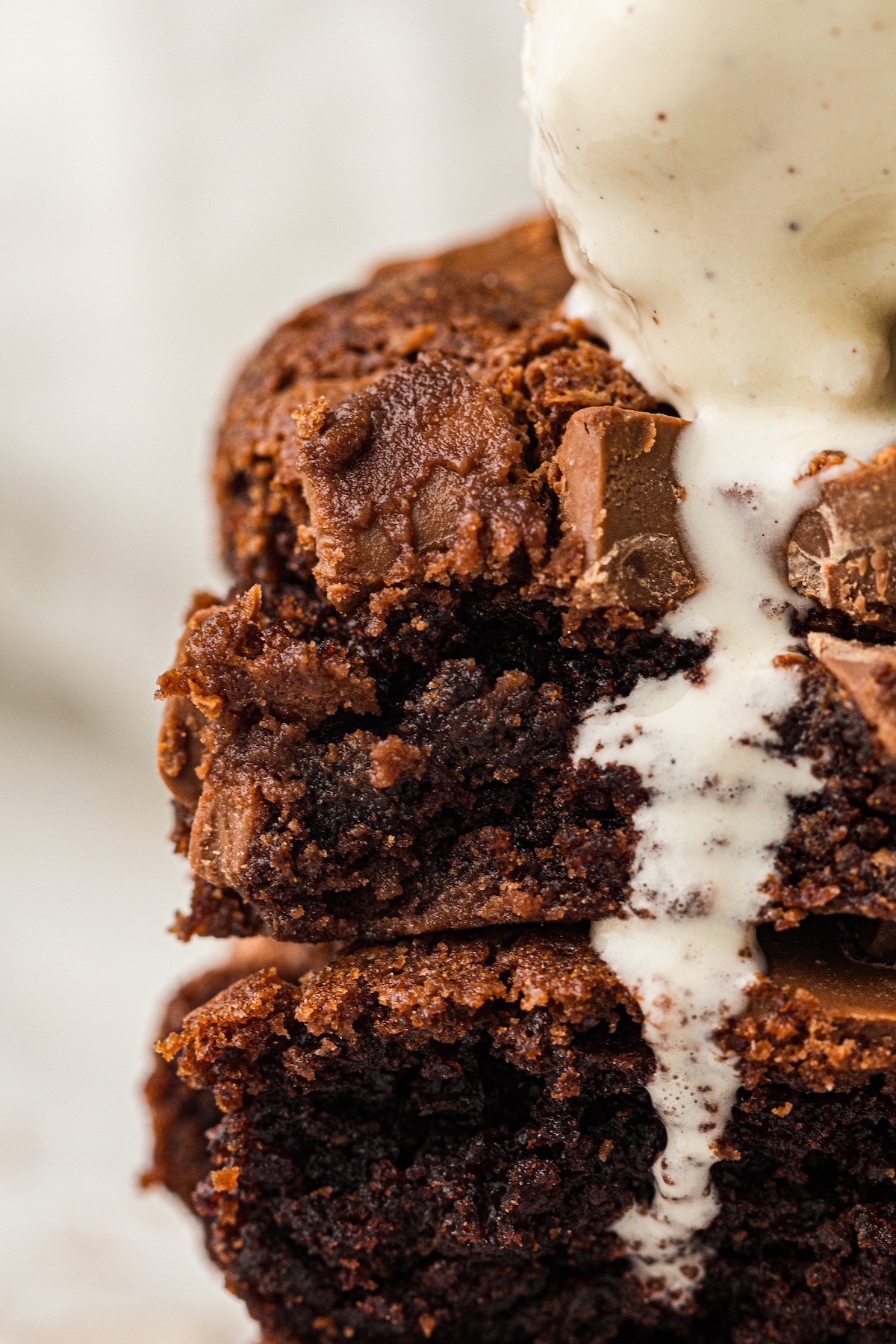 Close-up of a stack of three chocolate brownies topped with a scoop of vanilla bean ice cream. The brownies have a rich, fudgy texture with crinkly tops and are studded with milk chocolate chunks.