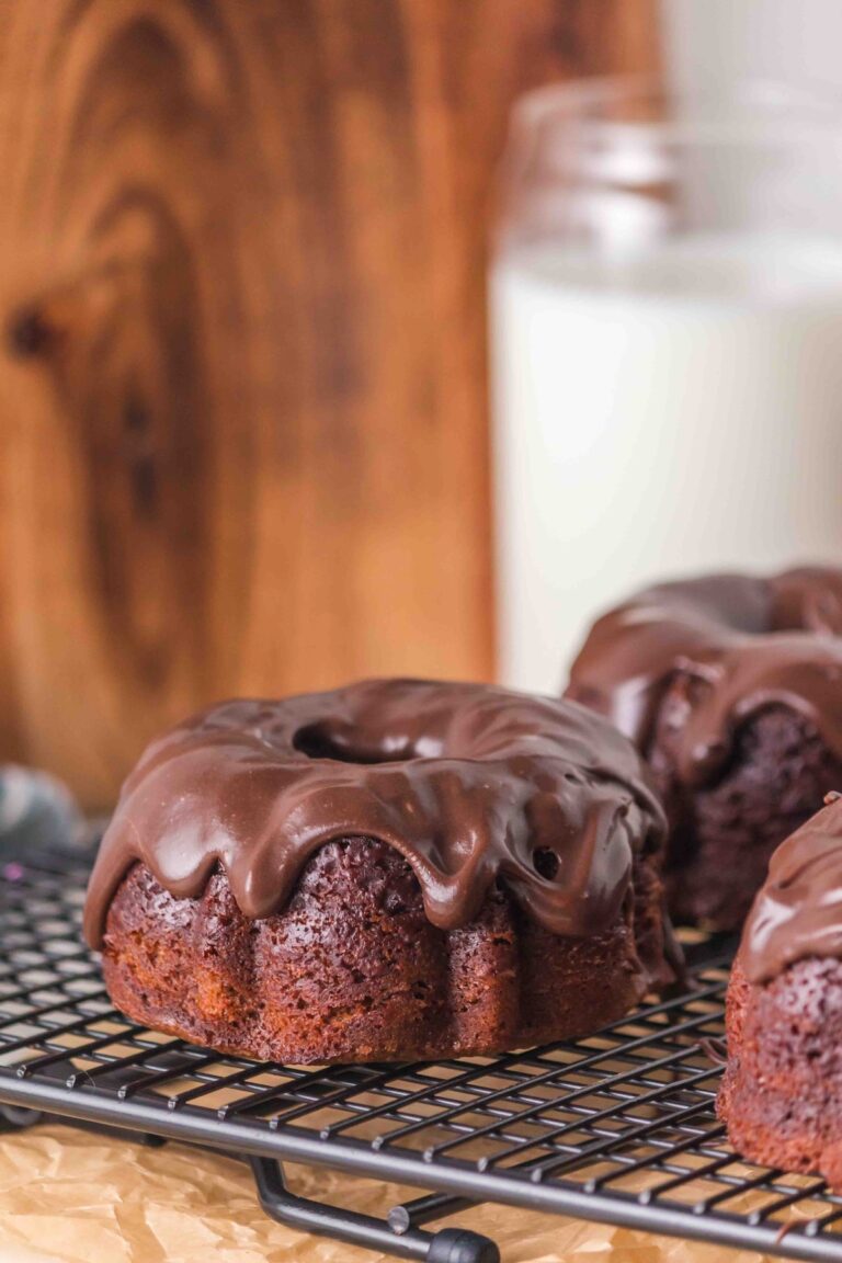 Glazed chocolate mini bundt cake on a cooling rack with a glass of milk in the background.