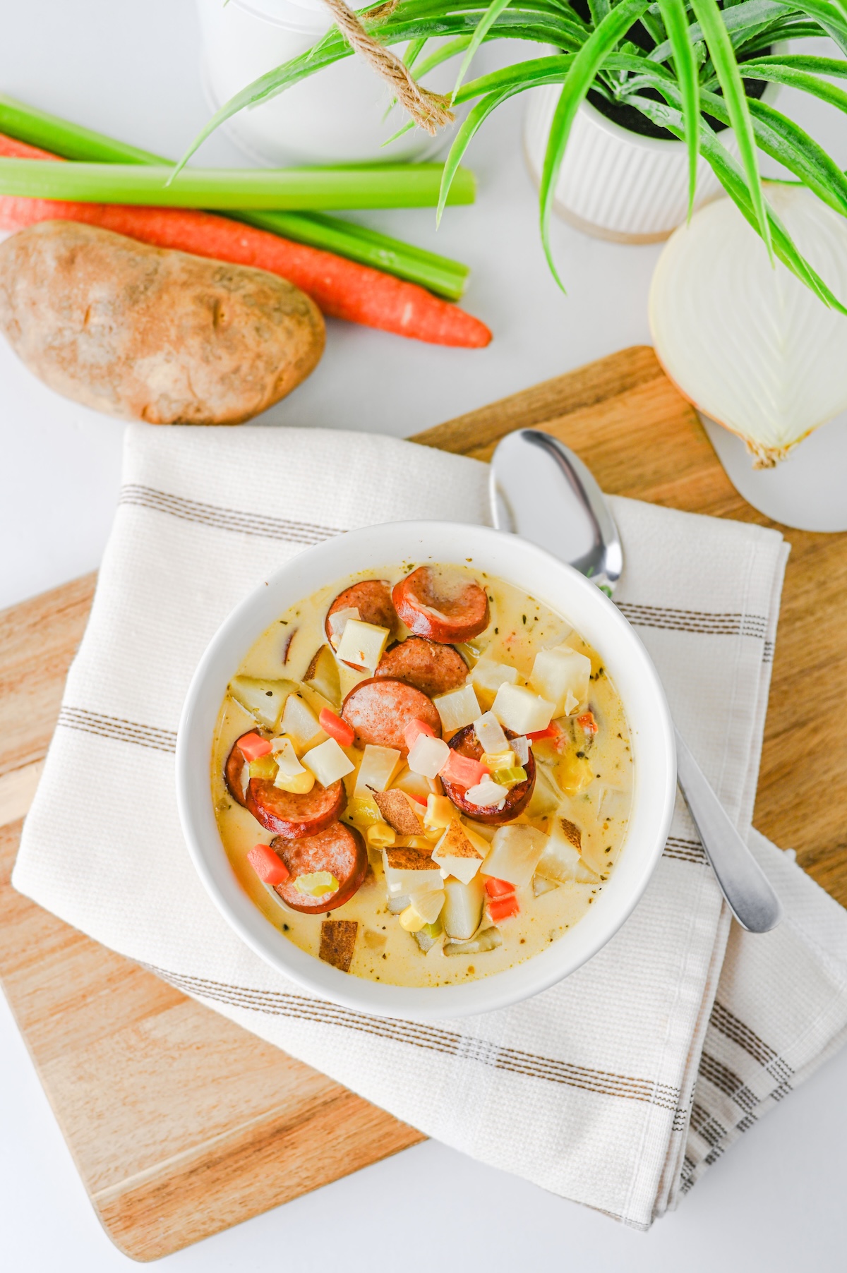 Top-down shot of creamy kielbasa potato soup with a spoon resting beside the bowl on a wooden cutting board.