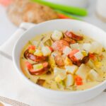 Close-up of kielbasa potato soup showing crispy sausage rounds, diced potatoes, carrots, and corn in a creamy broth.