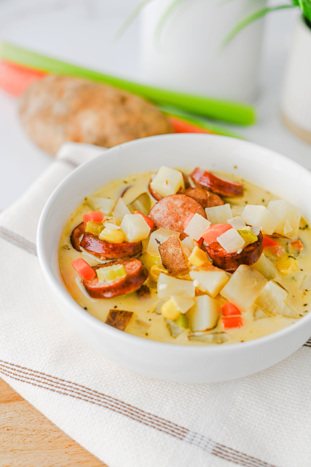 Close-up of kielbasa potato soup showing crispy sausage rounds, diced potatoes, carrots, and corn in a creamy broth.