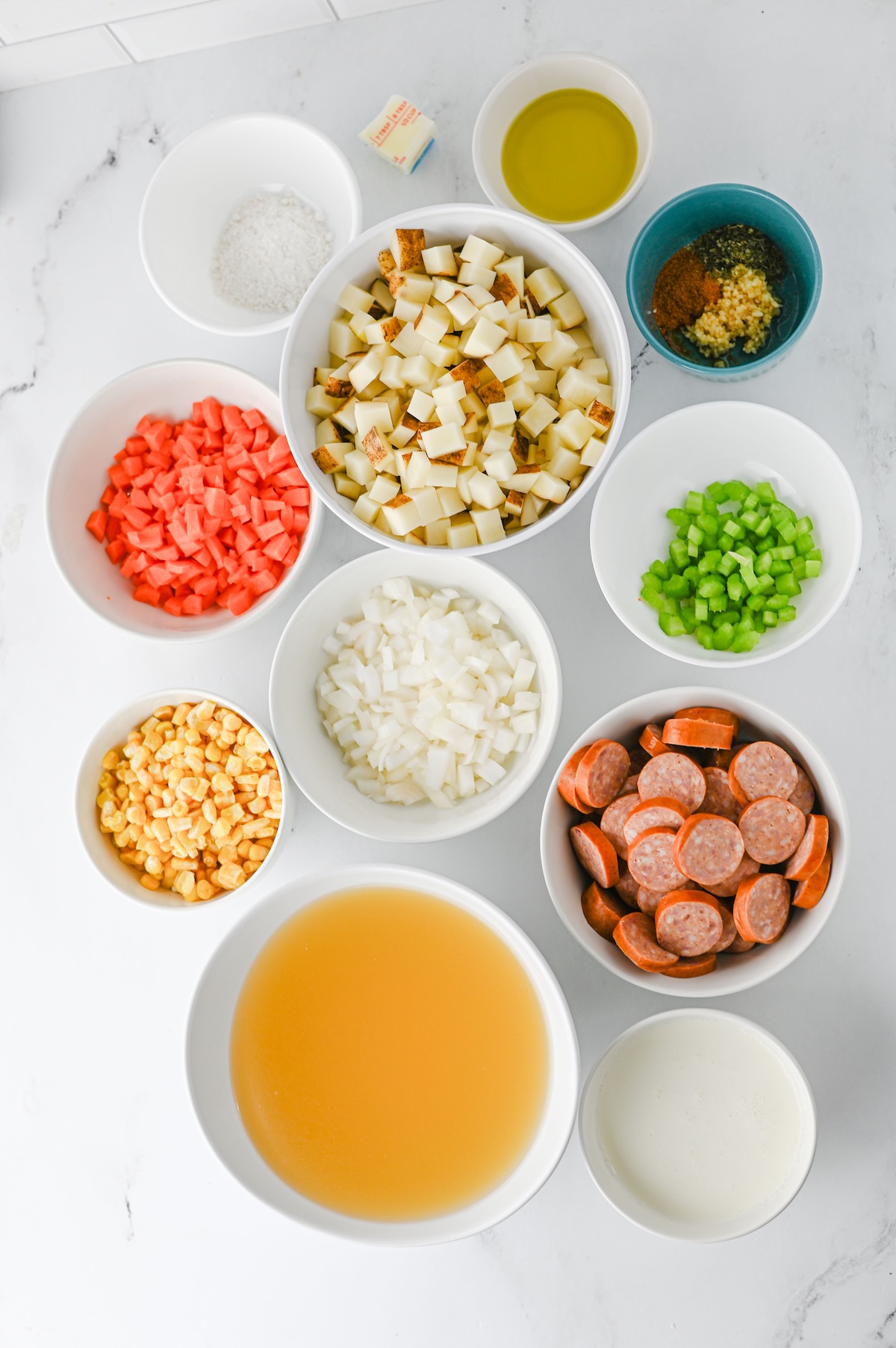 Overhead shot of prepped ingredients for kielbasa potato soup, including diced vegetables, sausage, broth, and cream in bowls.