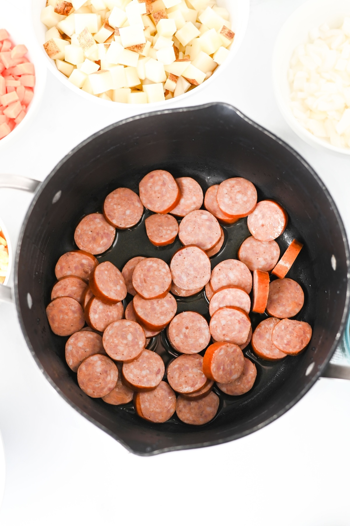 Sliced kielbasa sausage rounds searing in a black pot before the vegetables are added.