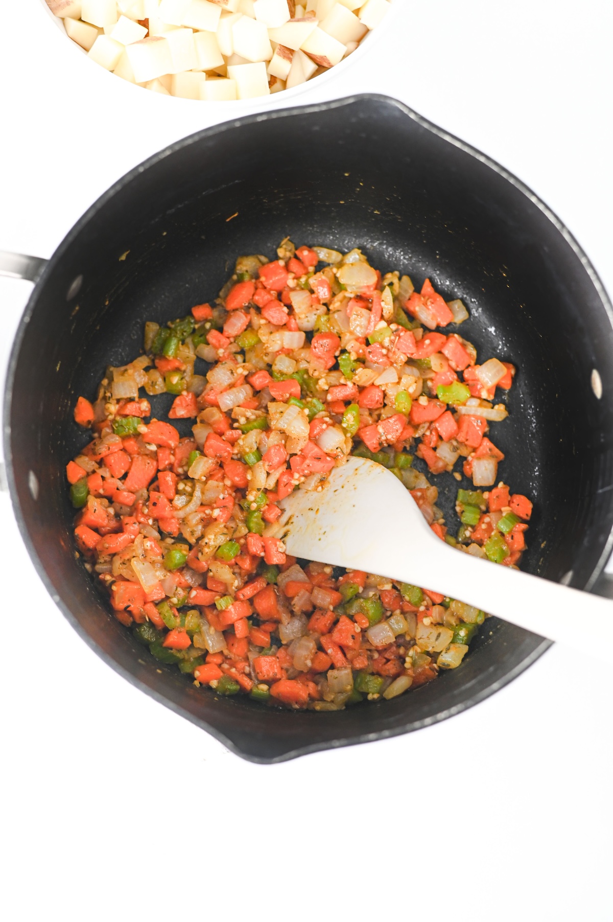 Softened onion, carrot, and celery seasoned with garlic and spices cooking in a pot.