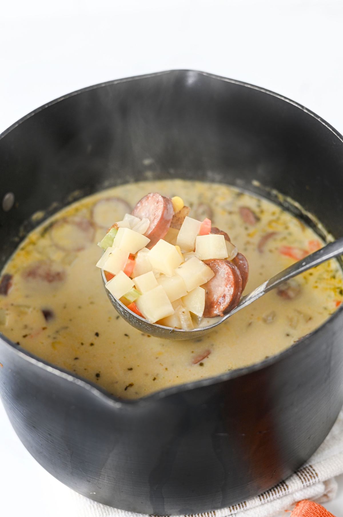 Ladle lifting a scoop of finished kielbasa potato soup from the pot, showing potatoes, sausage, and broth.