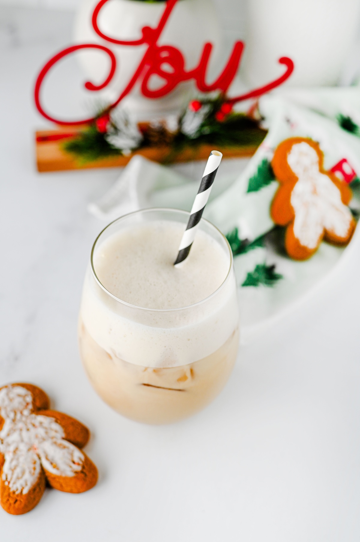 Iced gingerbread chai latte topped with oat milk foam beside frosted gingerbread man cookies