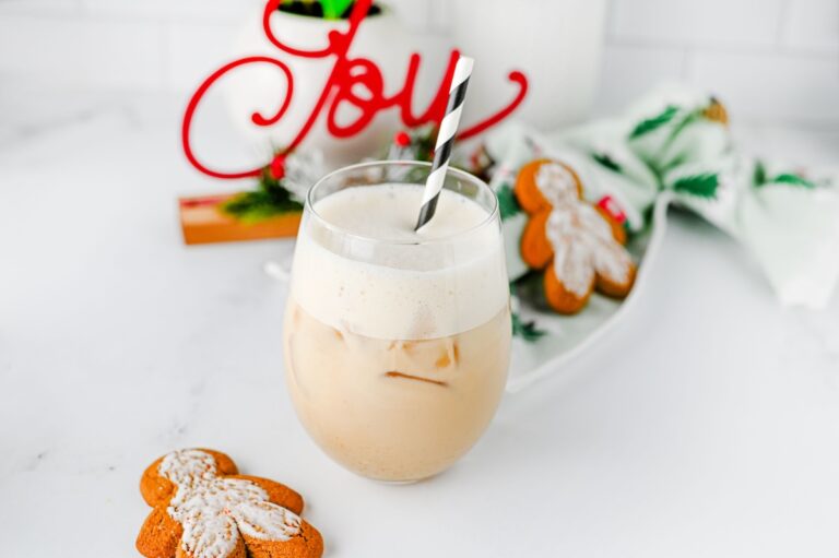 Iced gingerbread chai latte with a striped straw in front of holiday decor and gingerbread cookies
