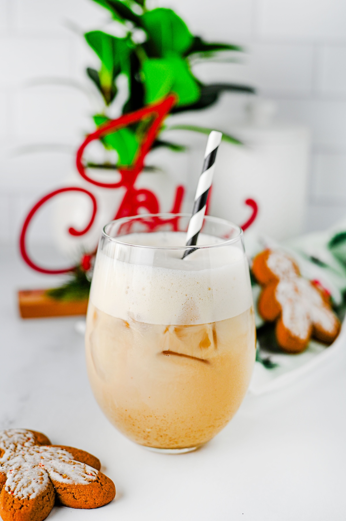 Close-up of an iced gingerbread chai latte with a thick layer of foam and a red Joy sign behind it