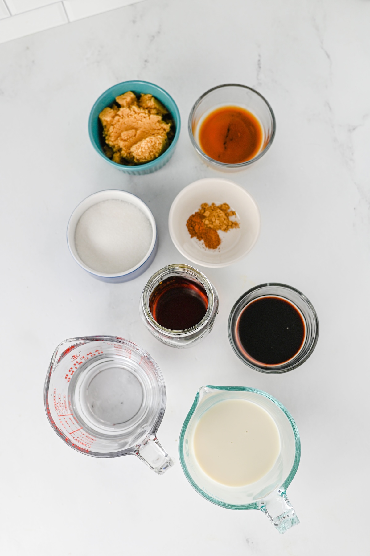 Ingredients for an iced gingerbread chai latte, including brown sugar, granulated sugar, spices, molasses, vanilla, chai concentrate, water, and oat milk