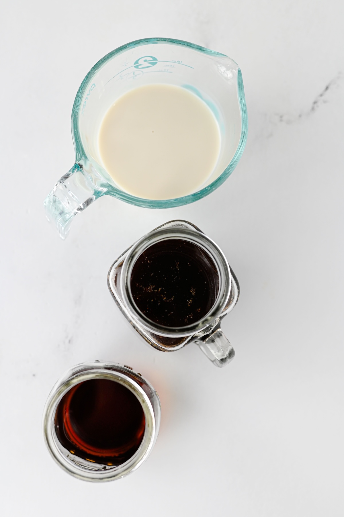 Homemade gingerbread syrup in a glass jar next to oat milk and chai concentrate