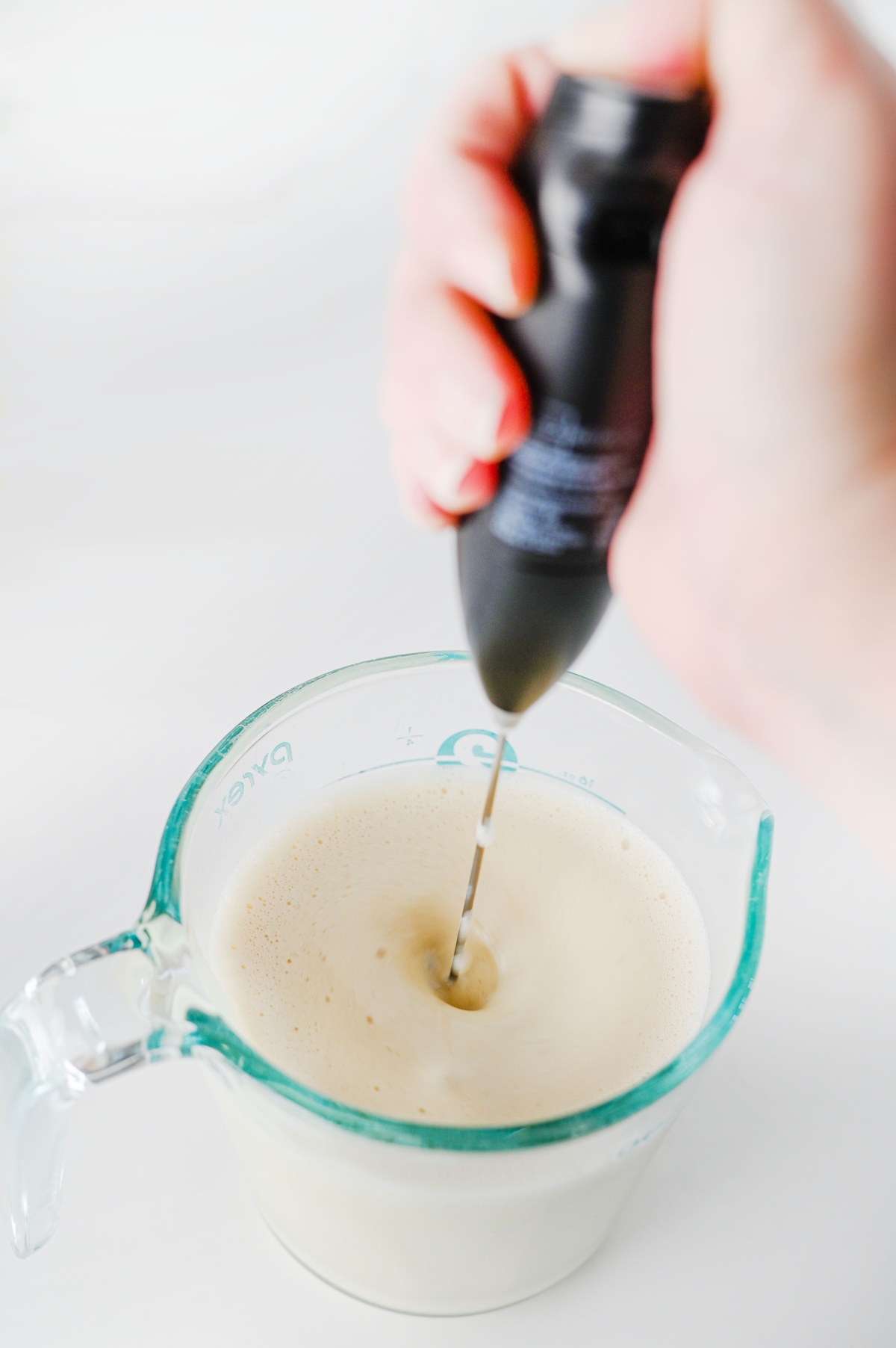 Hand frother foaming oat milk and gingerbread syrup in a glass measuring cup