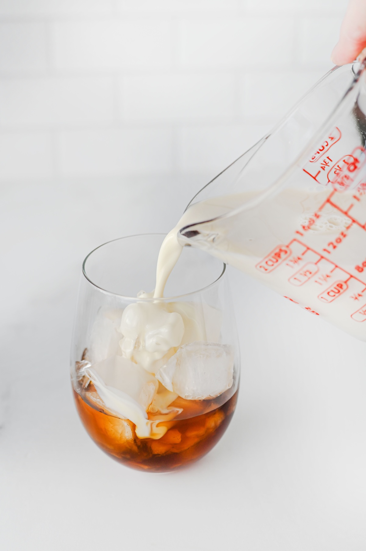 Oat milk being poured into a glass of chai concentrate over ice
