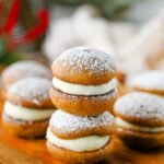Stacked gingerbread whoopie pies with creamy filling and powdered sugar on a wooden board