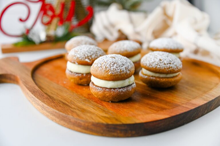Gingerbread whoopie pies on a wooden serving board with a red Joy sign and holiday greenery in the background