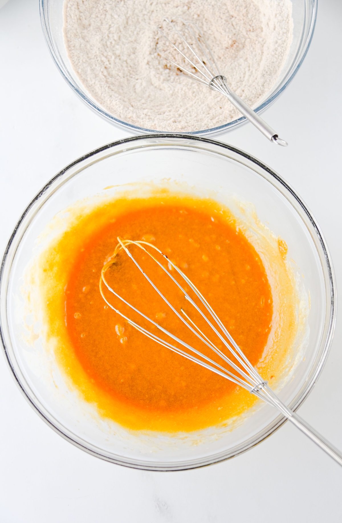 Whisked wet ingredients in a glass bowl next to the bowl of dry ingredients