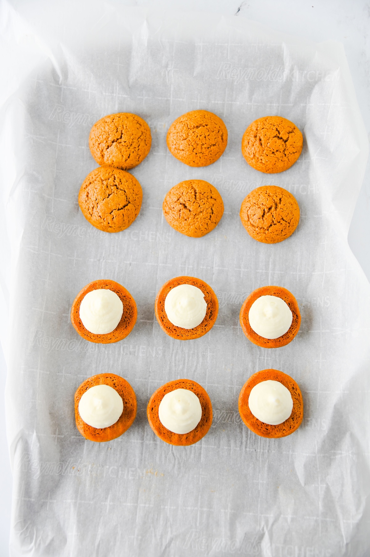 Cream cheese filling piped onto half of the gingerbread cookies on a baking sheet