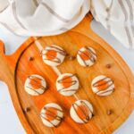 Overhead view of caramel-filled thumbprint cookies with chocolate drizzle on a pumpkin-shaped cutting board