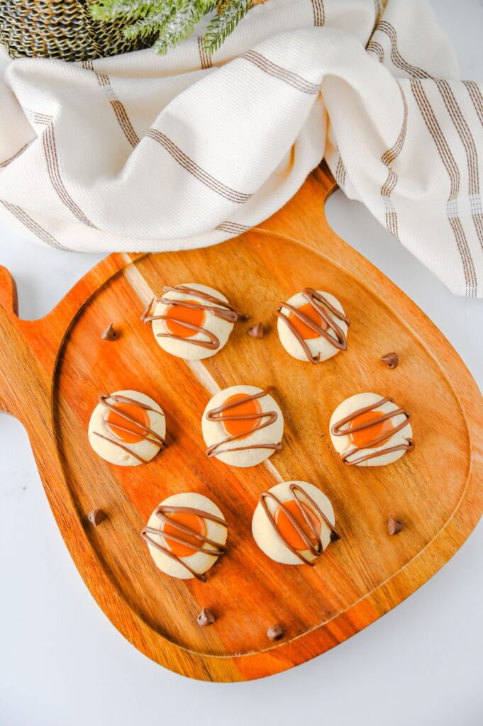 Overhead view of caramel-filled thumbprint cookies with chocolate drizzle on a pumpkin-shaped cutting board