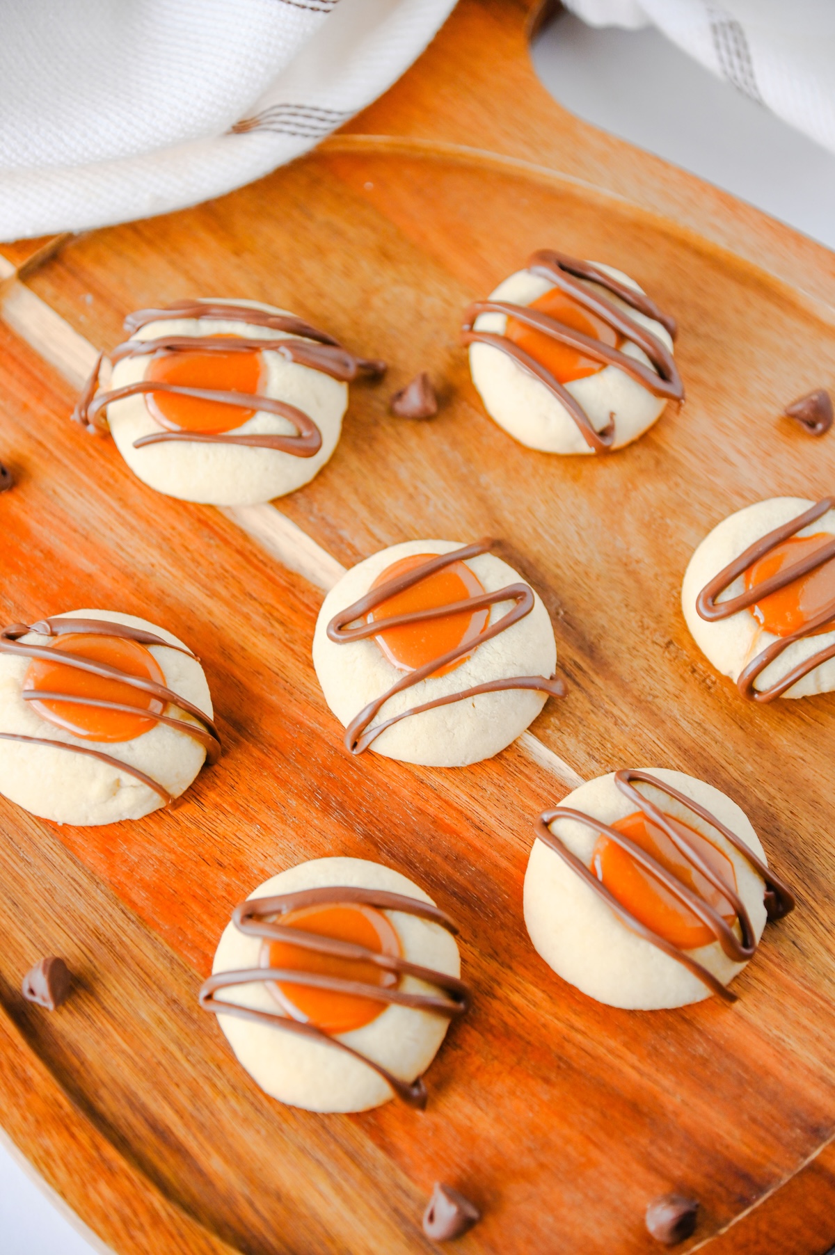 Overhead close-up of caramel-filled Twix thumbprint cookies with chocolate chips scattered around
