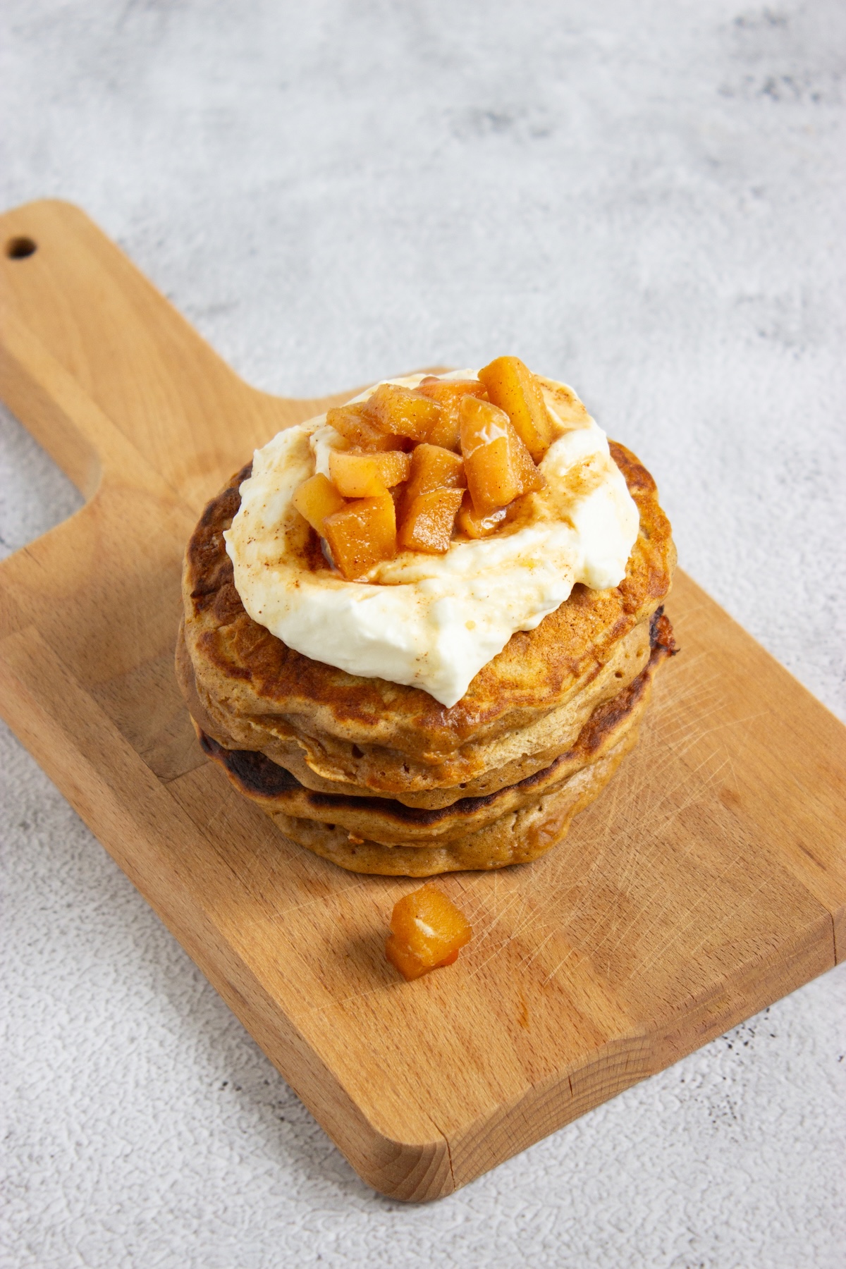 Stack of apple cinnamon pancakes topped with whipped cream and caramel apple compote on a wooden serving board