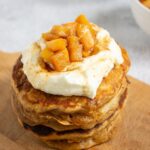 Close-up of a tall stack of fluffy apple cinnamon pancakes topped with whipped cream and caramel apple compote