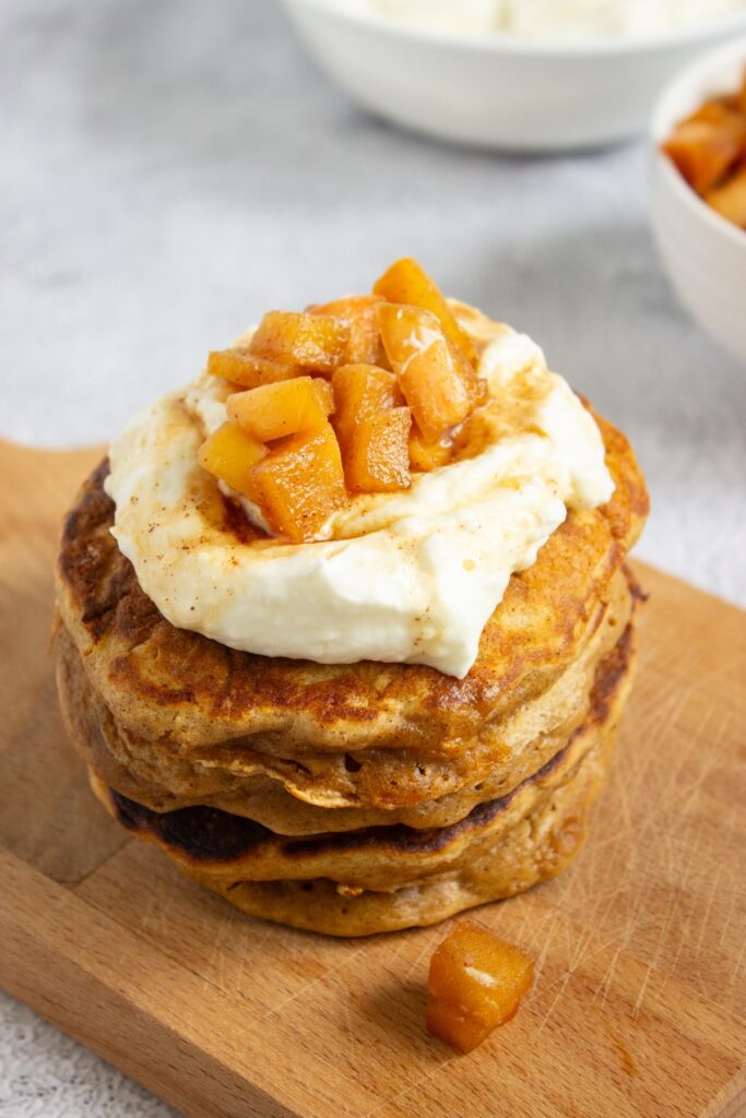 Close-up of a tall stack of fluffy apple cinnamon pancakes topped with whipped cream and caramel apple compote