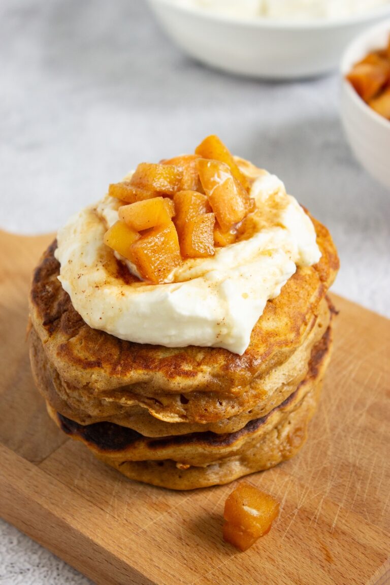 Close-up of a tall stack of fluffy apple cinnamon pancakes topped with whipped cream and caramel apple compote