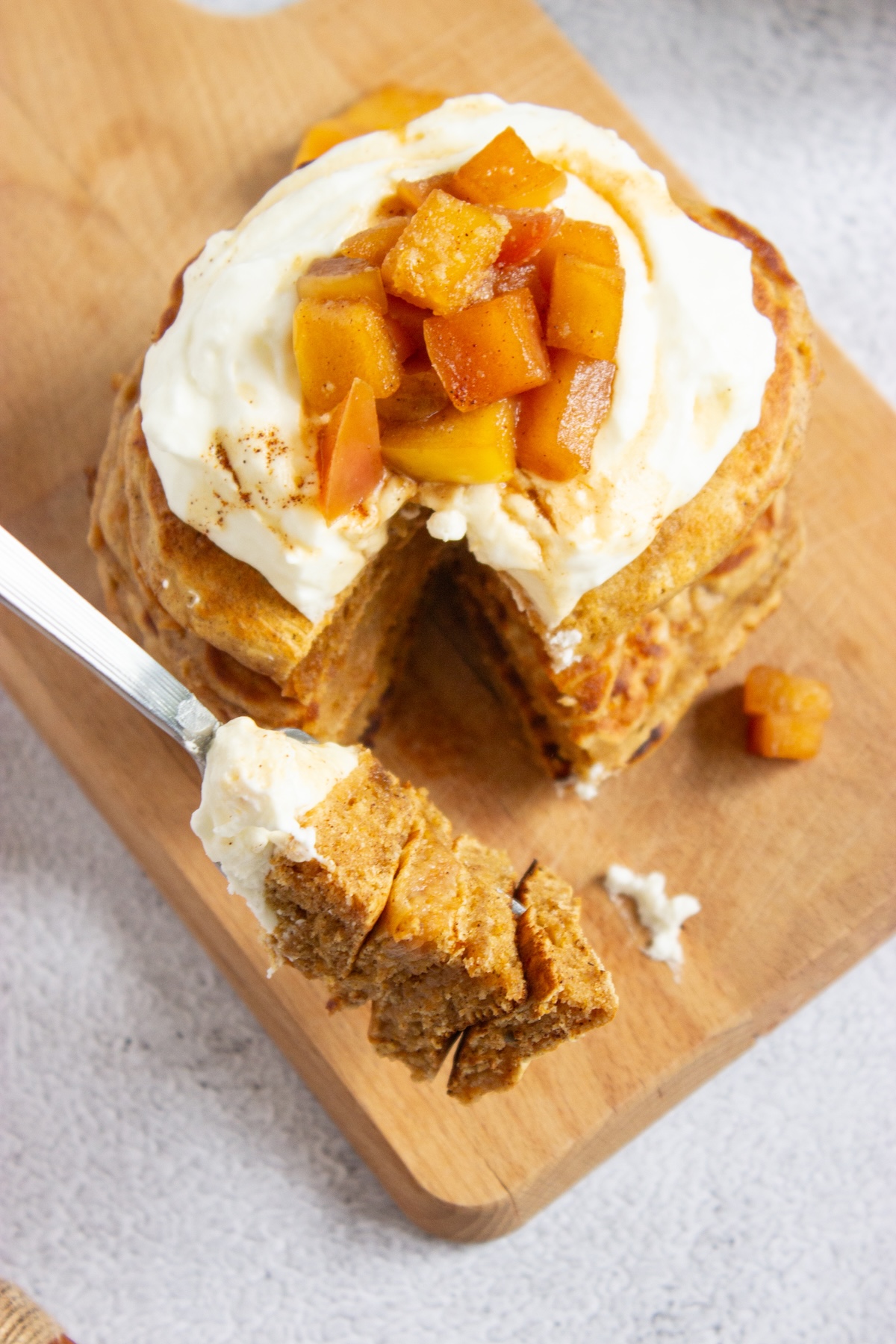 Forkful of fluffy apple cinnamon pancakes cut from a stack topped with whipped cream and caramel apple compote