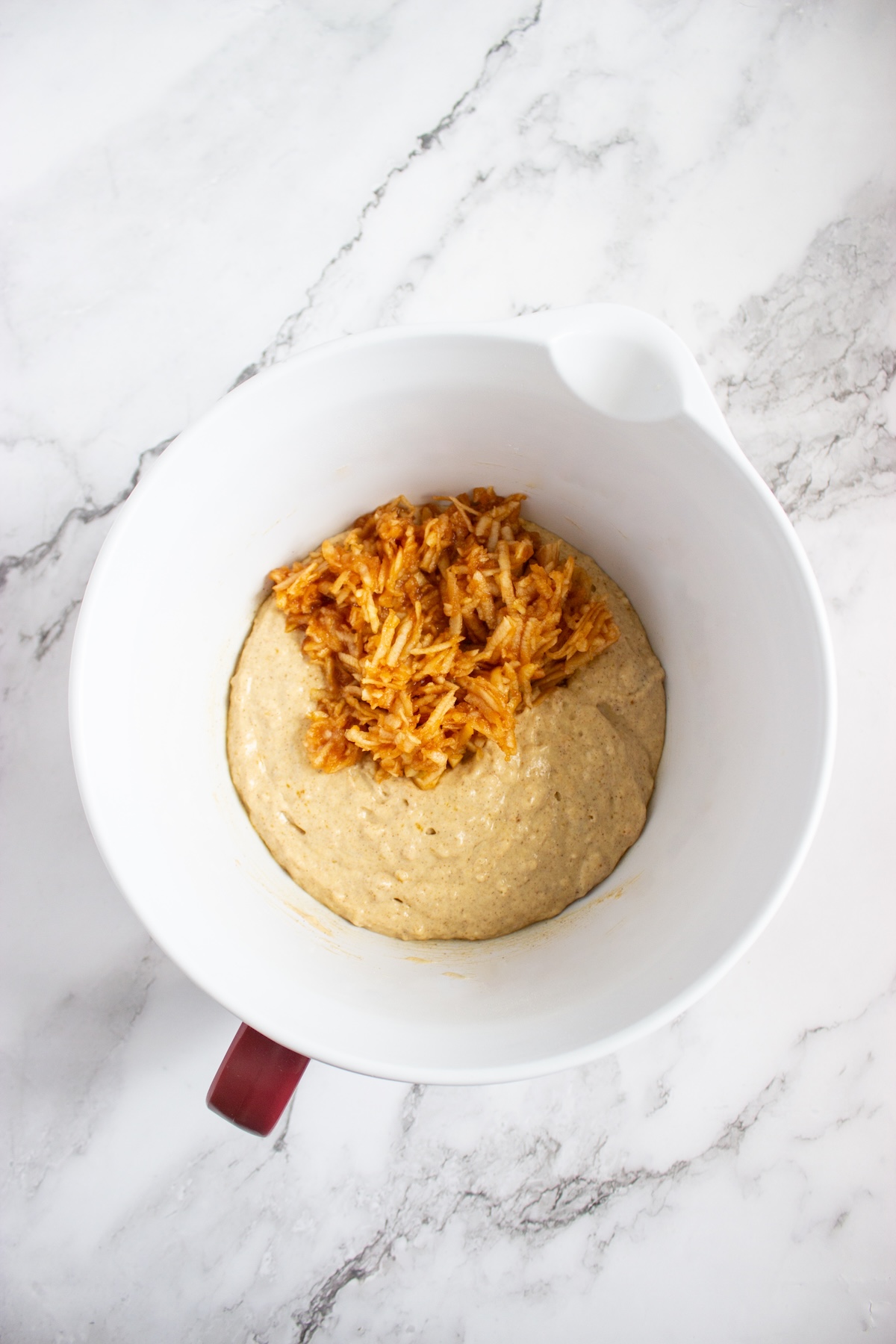 Grated apple added on top of pancake batter in a white mixing bowl