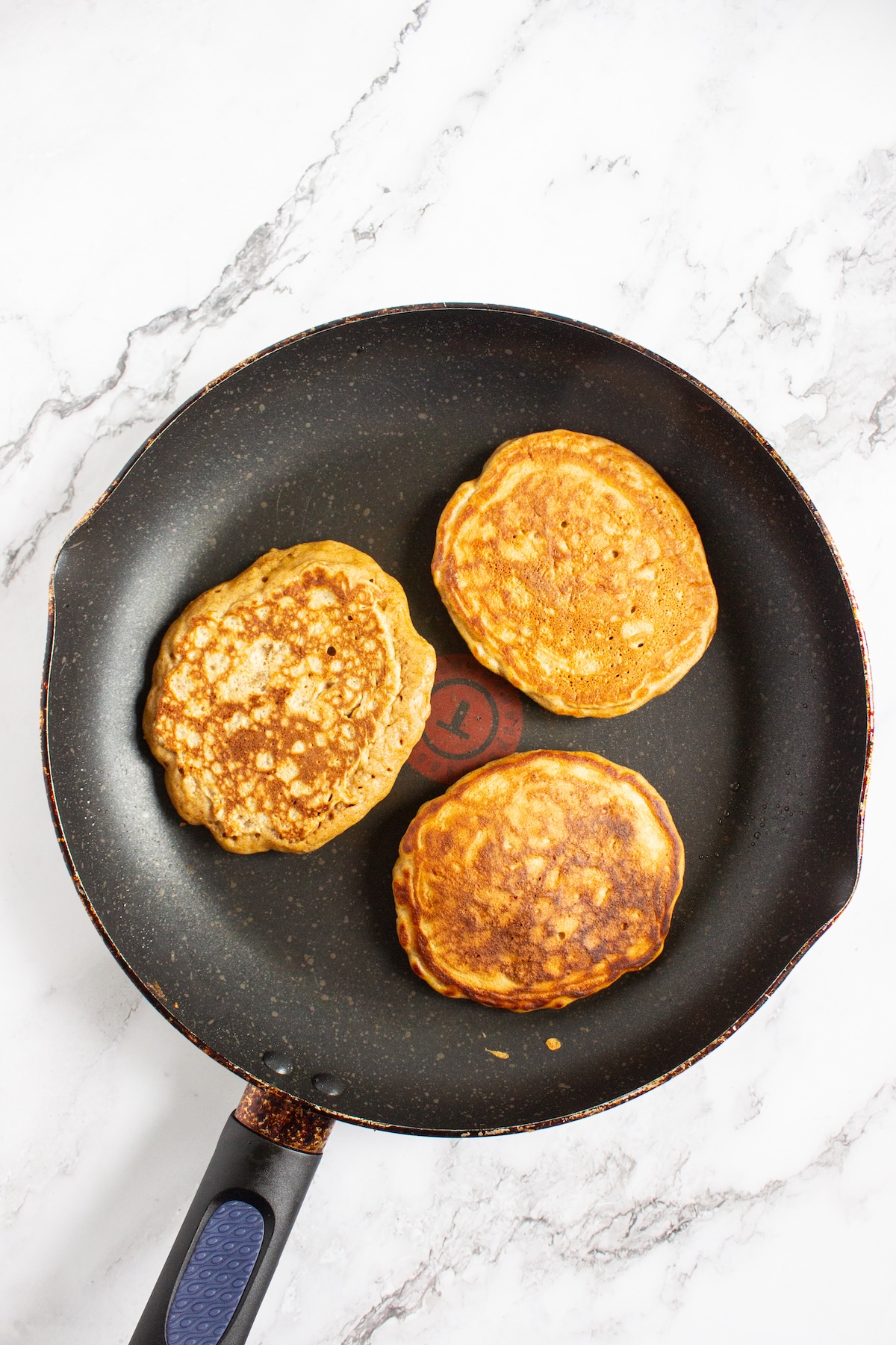 Three apple cinnamon pancakes cooking in a nonstick skillet