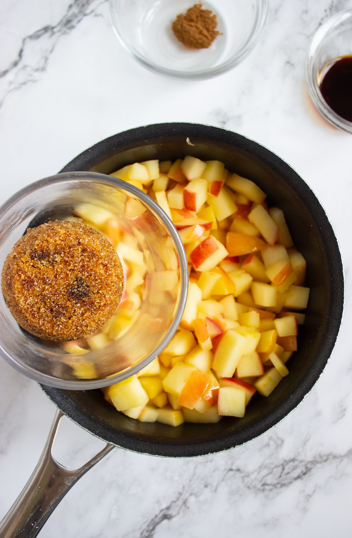 Brown sugar being added to diced apples in a saucepan