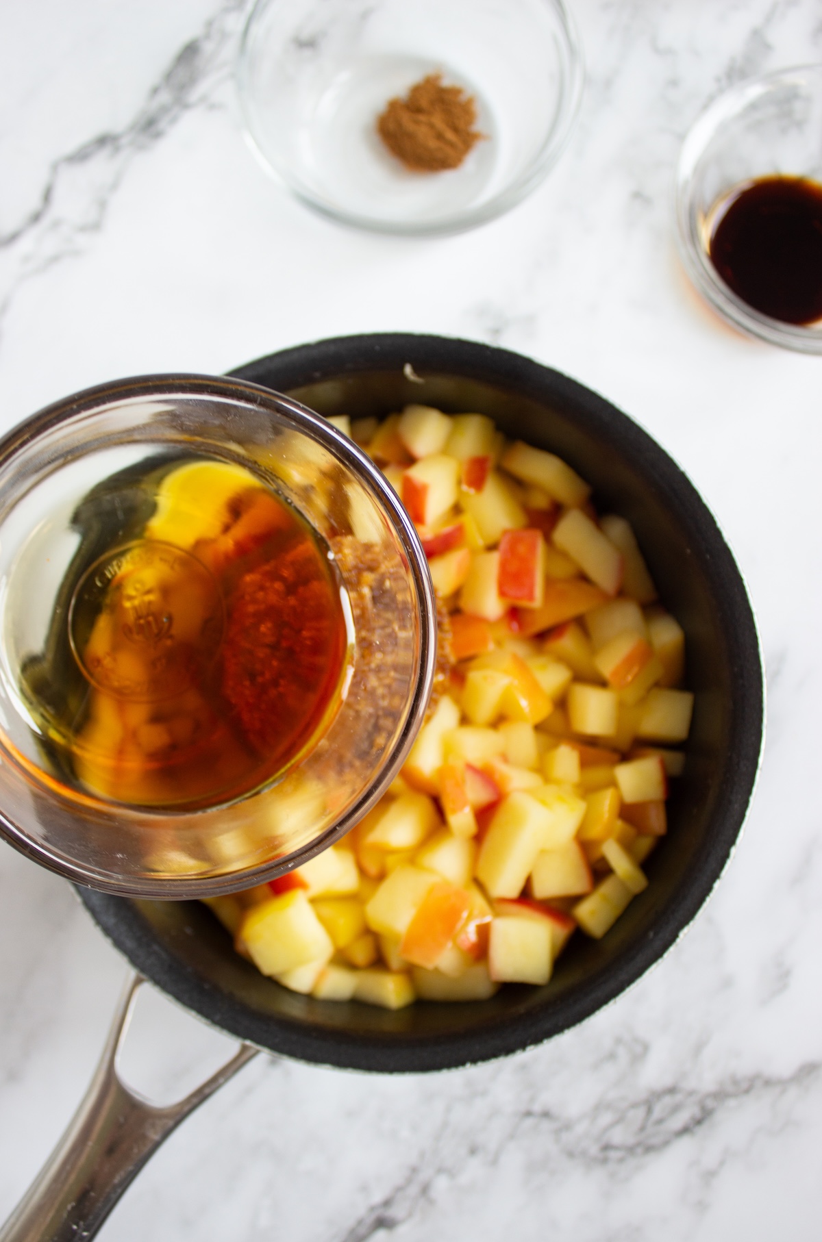 Maple syrup being poured over diced apples in a saucepan