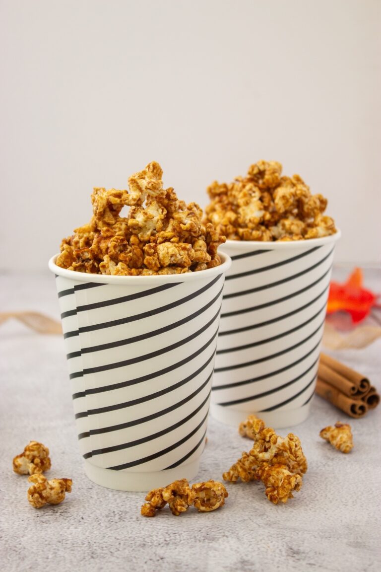 Brown butter maple popcorn in two striped paper cups with cinnamon sticks and fall leaves