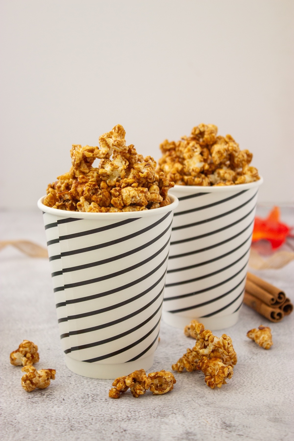 Brown butter maple popcorn in two striped paper cups with cinnamon sticks and fall leaves