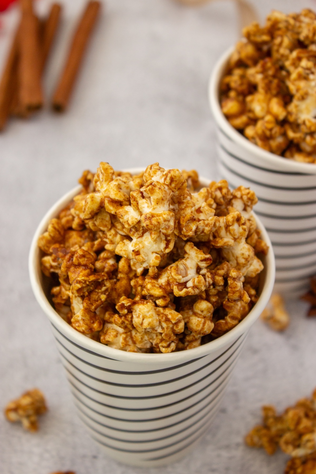 Striped cup filled with brown butter maple popcorn beside cinnamon sticks