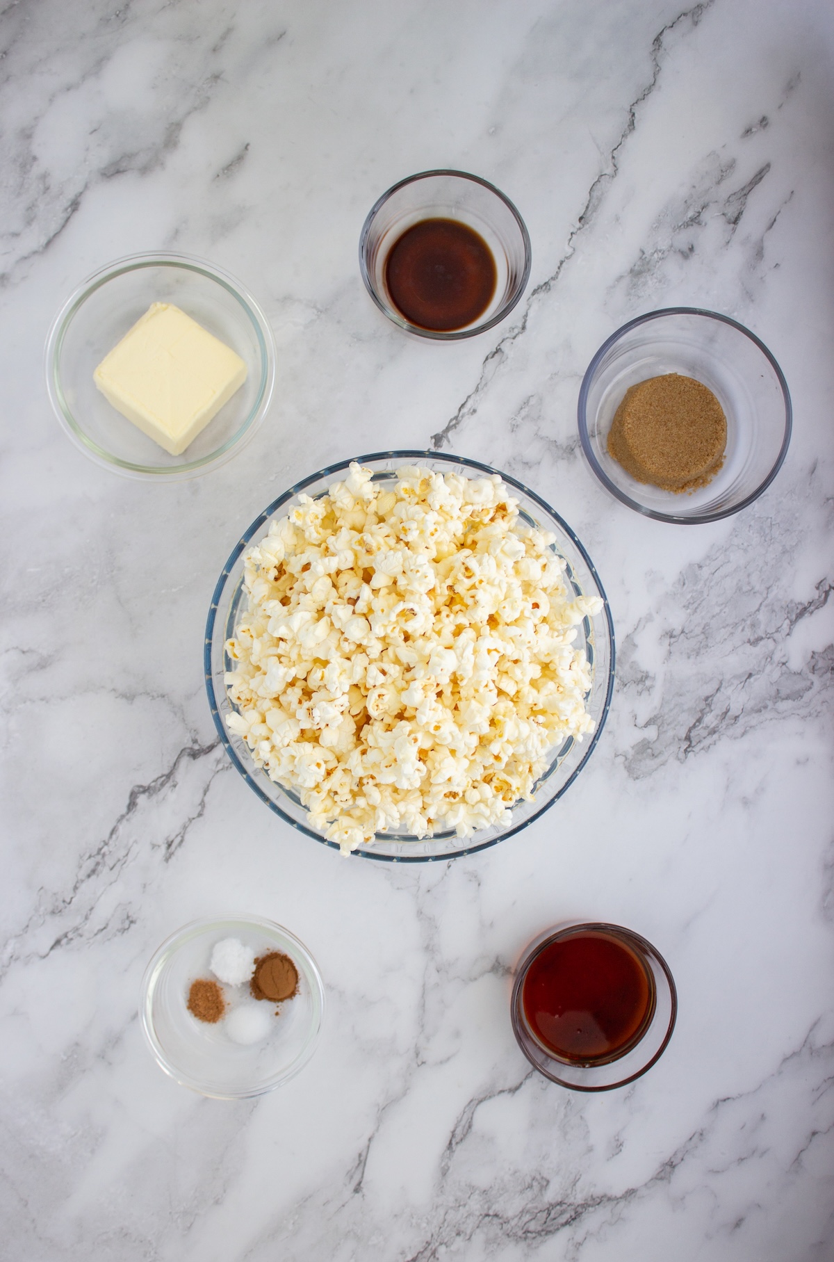 Ingredients for brown butter maple popcorn including popped popcorn, butter, maple syrup, brown sugar, vanilla, and spices