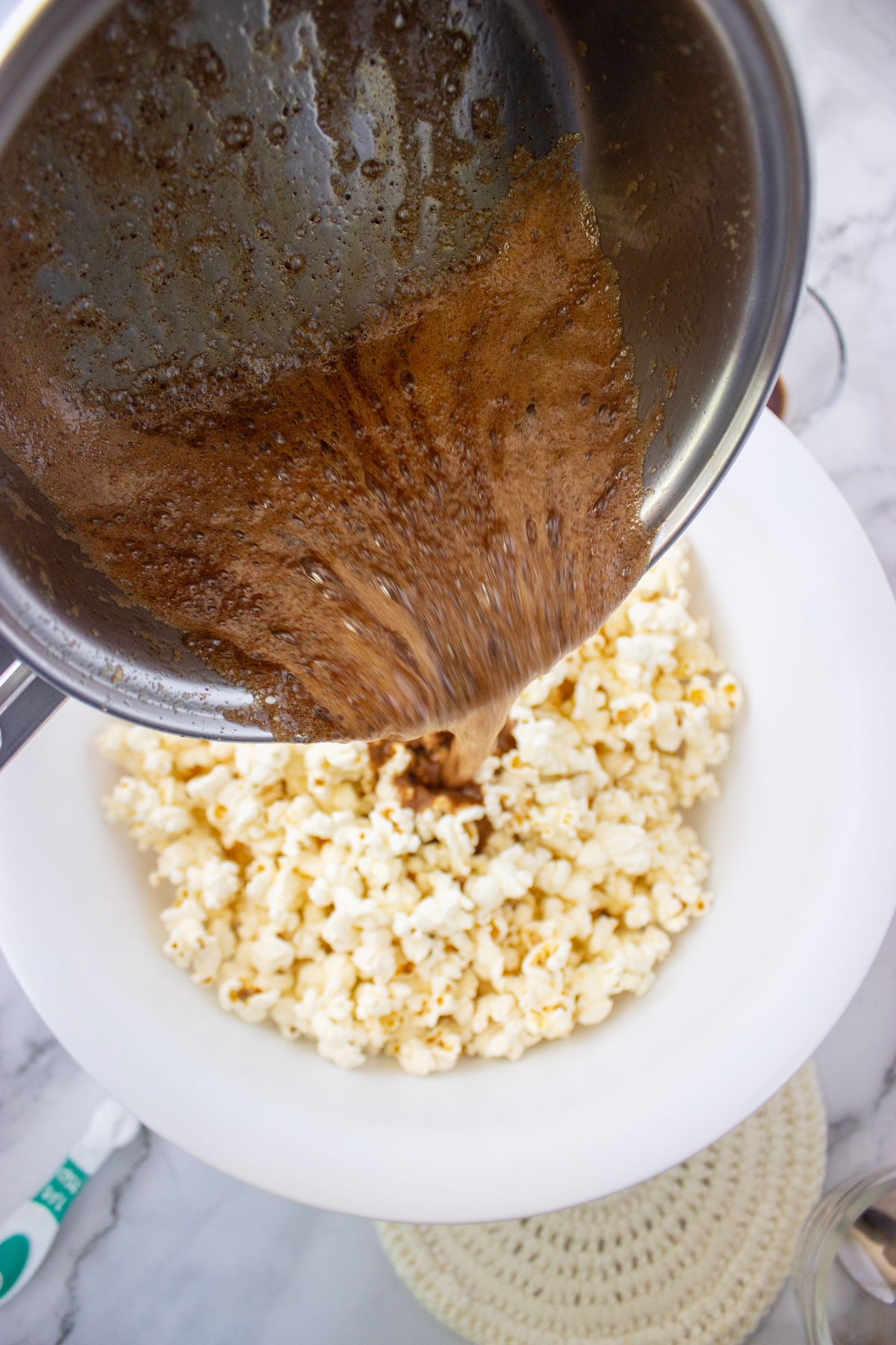 Pouring maple caramel sauce onto a bowl of plain popped popcorn