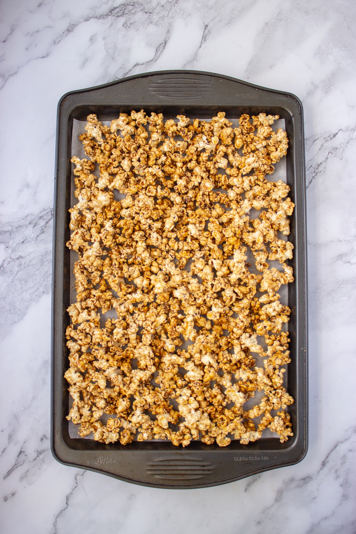 Maple caramel coated popcorn spread on a baking sheet