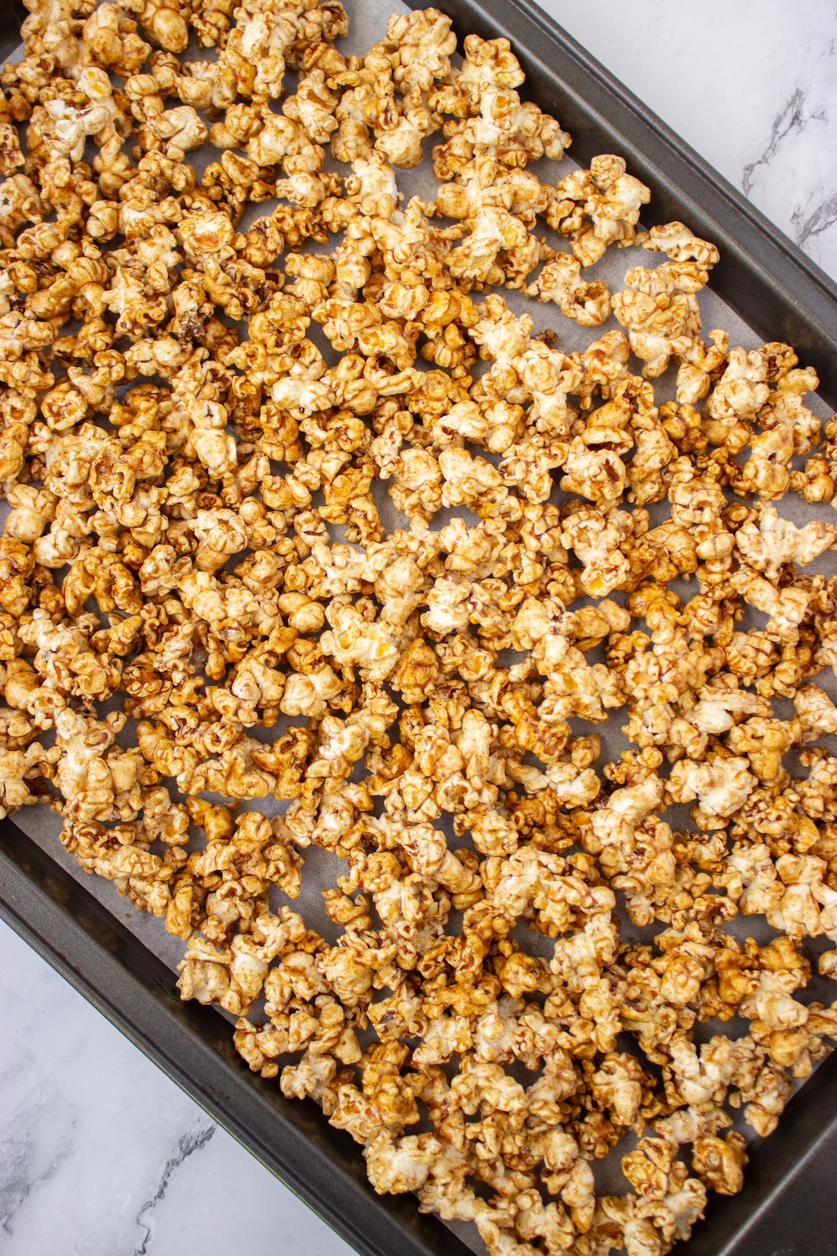 Close-up of caramel-coated popcorn spread in a single layer on a baking sheet