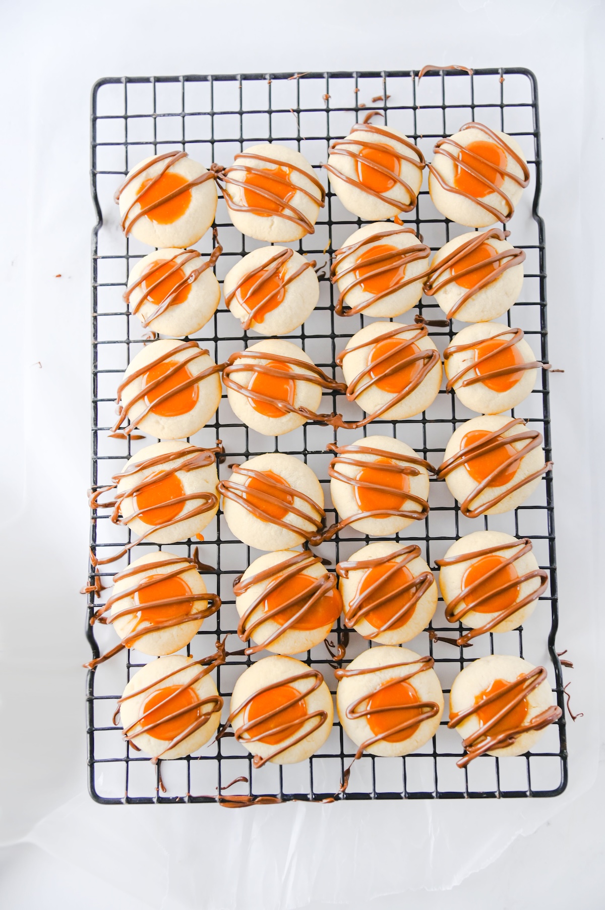 Twix thumbprint cookies with caramel centers and chocolate drizzle on a wire rack