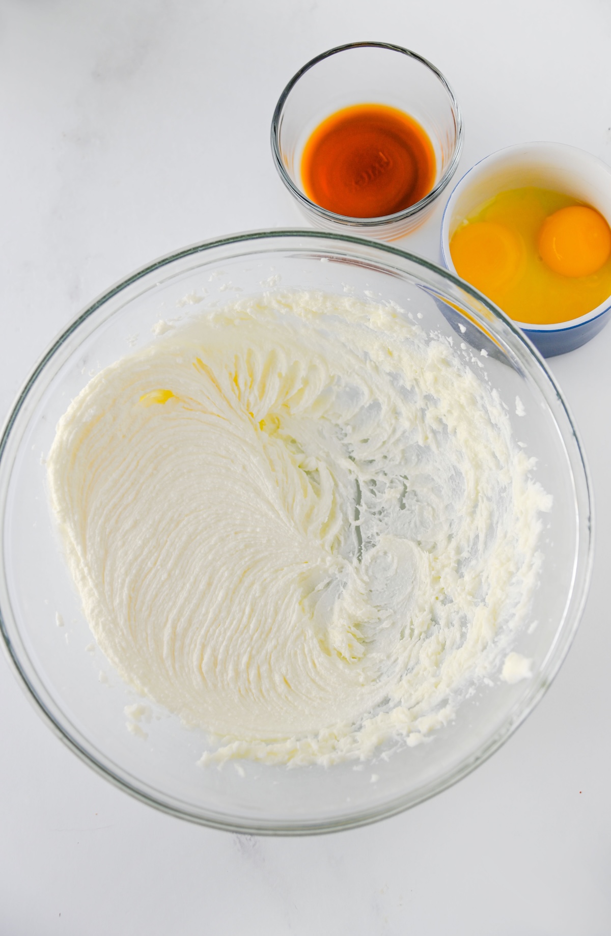 Creamed butter and sugar in a glass bowl with vanilla and egg yolks nearby