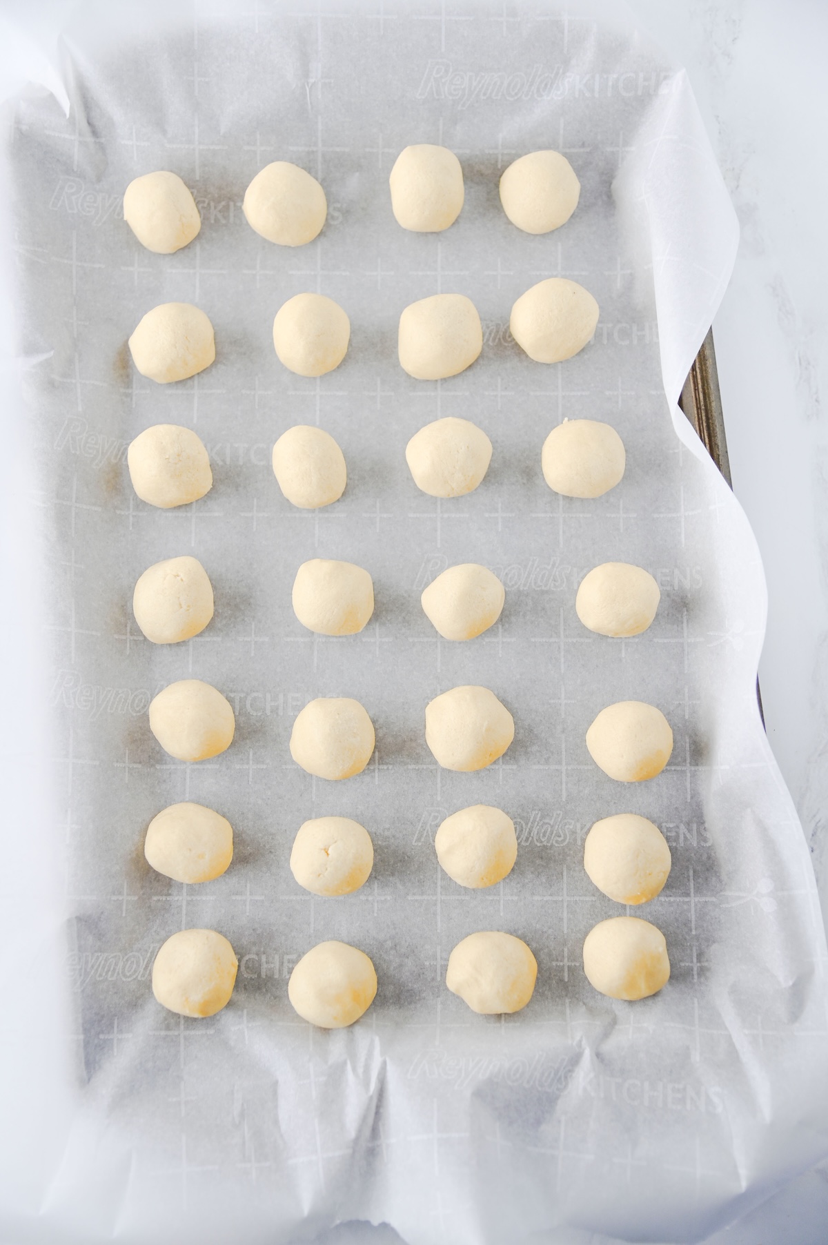 Rolled cookie dough balls lined up on a parchment-lined baking sheet