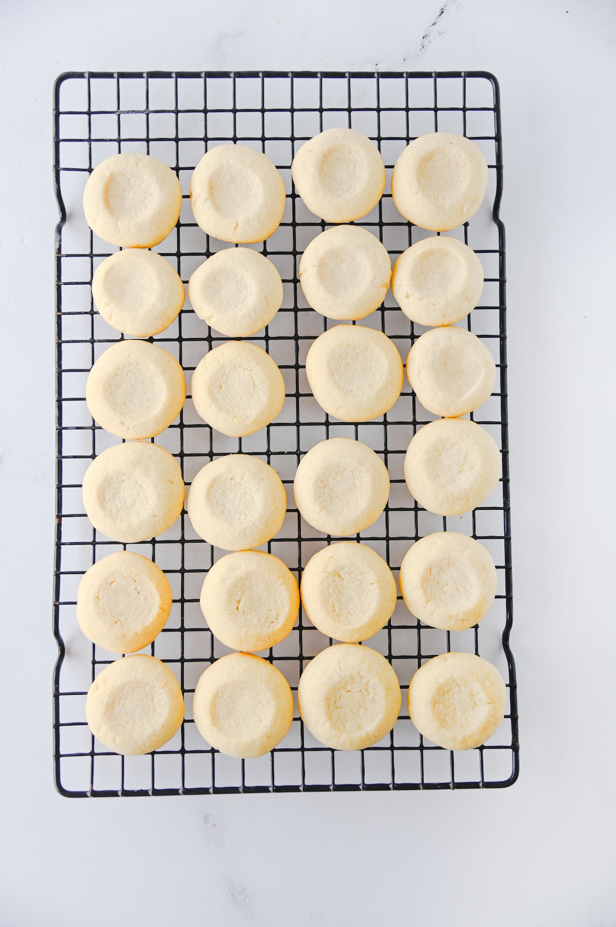 Baked thumbprint cookies cooling on a black wire rack