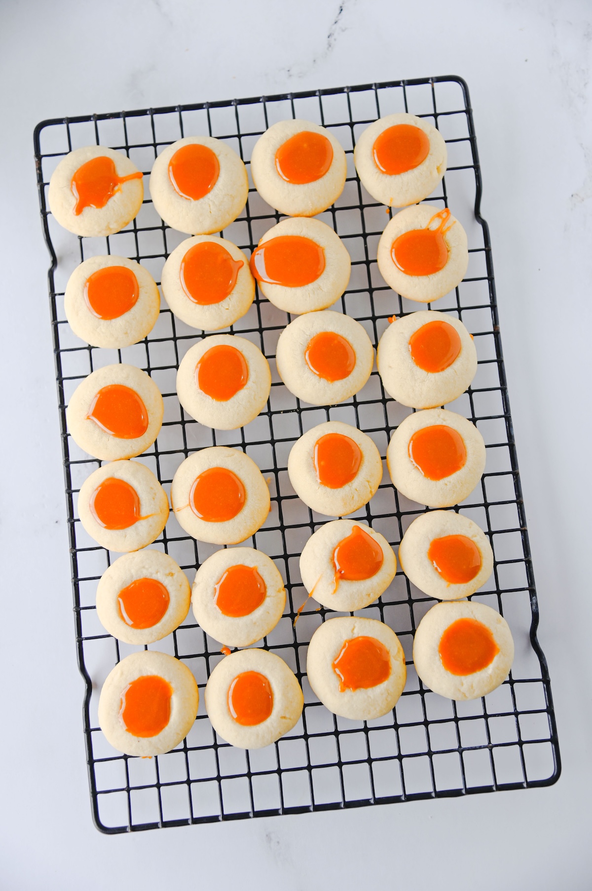 Thumbprint cookies filled with caramel cooling on a wire rack