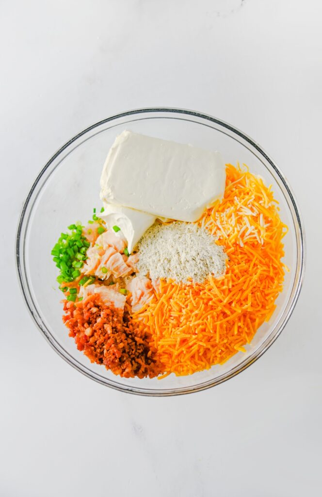 Chicken, cream cheese, sour cream, ranch seasoning, bacon, shredded cheese, and green onions in a glass mixing bowl